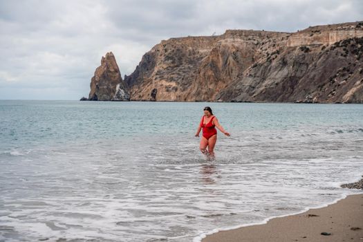 Woman in a bathing suit at the sea. A fat young woman in a red swimsuit enters the water during the surf.