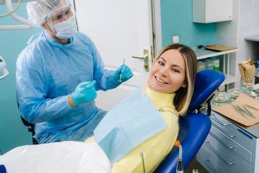 The patient smiles in the dentist's chair in a protective mask and instrument before treatment in the dental office.