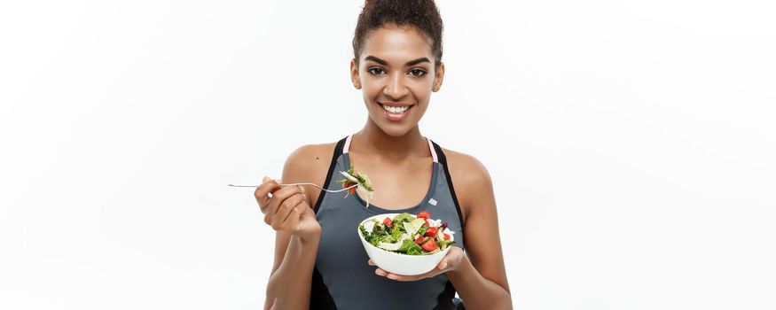 Healthy and Fitness concept - Beautiful American African lady in fitness clothes on diet eating fresh salad. Isolated on white background