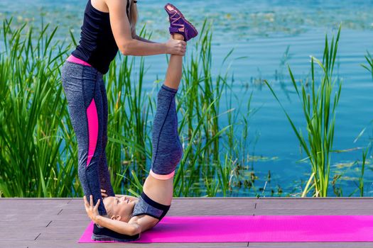 Little girt and woman are doing exercises on the grass at the shore of the lake.