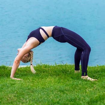 Healthy woman is stretching on the grass at the shore of the lake.