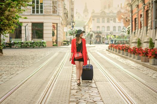 Beautiful young business woman walking on the tram track of a city street with blue travel bag.