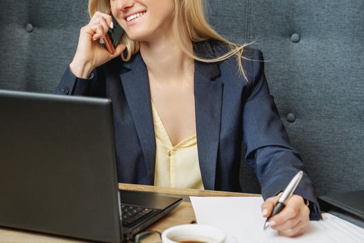 Beautiful young smiling woman is talking on the cell phone working on a laptop in home office.