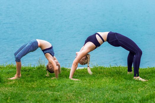 Mother and daughter doing exercise at the shore outdoors. Healthy lifestyle.