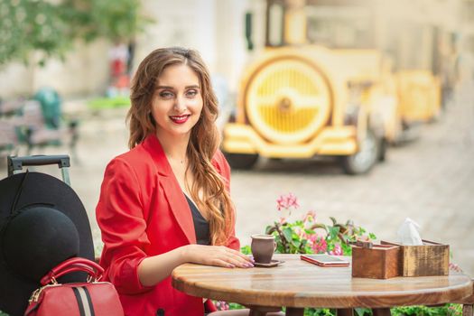 Portrait of smiling adorable girl with cup of coffee at the table in stylish outdoor cafe on the city street.