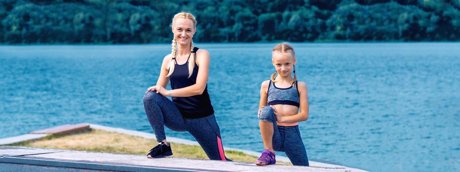 Portrait of mother and child in sport style clothes on the shore of the lake.