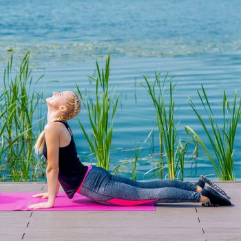 Healthy woman is stretching on the grass at the shore of the lake.