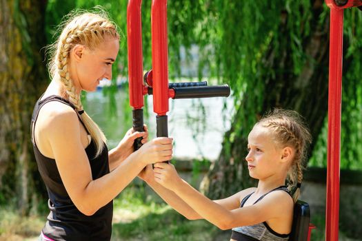 A little girl is training on public street simulator with young woman coach in the park.