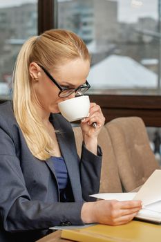 Business woman reading news working with documents and drinking coffee in office.