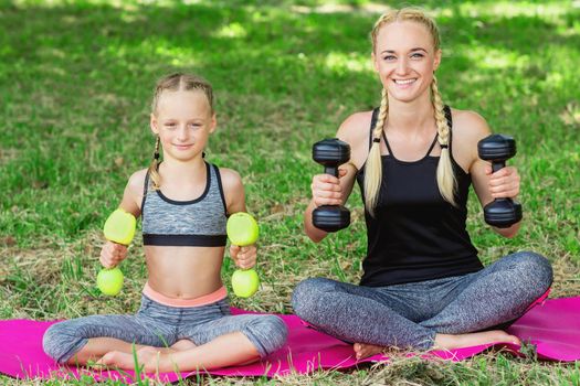 Young mother with her little daughter are training with apple dumbbells in the park.