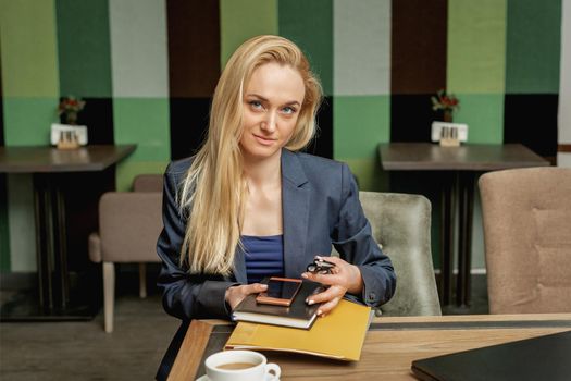 Portrait of beautiful young business woman holding office supplies sitting in office.