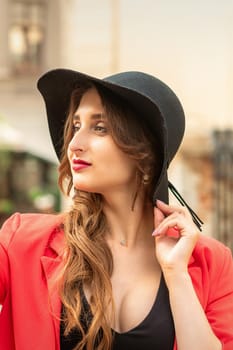 Side view of fashionable young woman in red coat and black hat looking away on the city street.
