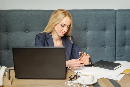 Young woman is using smartphone sitting at wooden table in coffee shop.