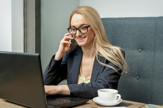 Young business woman with glasses having phone call sitting at the table in the home office.