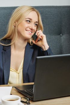 Business Woman in black suit is talking by mobile phone in home office.