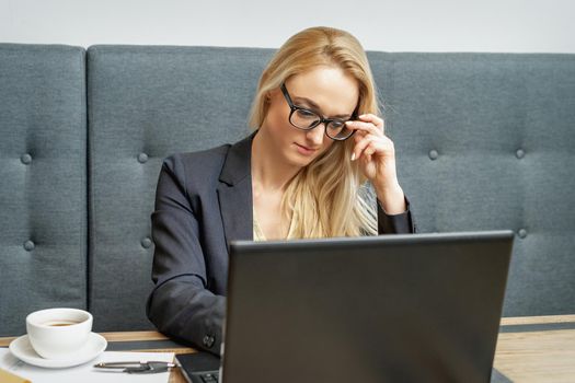 Busy business woman wearing eyeglasses working on laptop at home office.