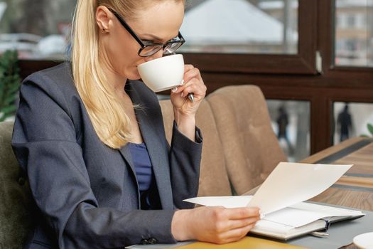 Business woman reading news working with documents and drinking coffee in office.