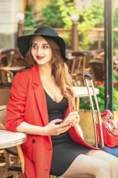 Portrait of attractive young woman holding smartphone in cafe outdoors.