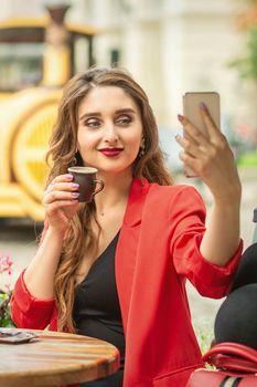 Young caucasian woman taking self portrait in outdoor cafe with cup of coffee.