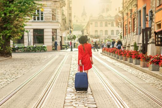 Beautiful young business woman walking on the tram track of a city street with blue travel bag.