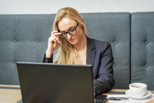 Busy business woman wearing eyeglasses working on laptop at home office.