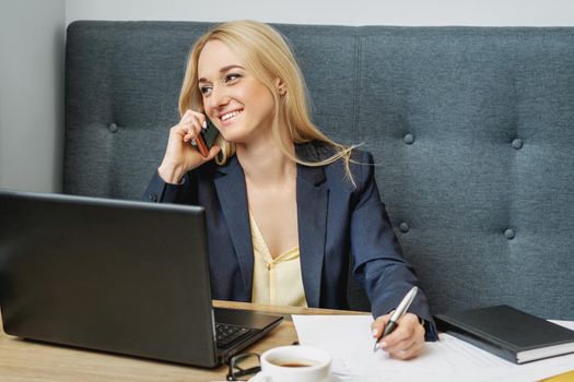 Young business woman is having phone call sitting at the table in the home office.