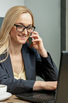 Business Woman in black suit with glasses is talking by mobile phone in home office.