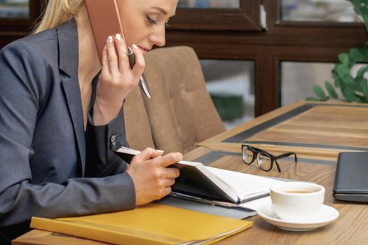 Beautiful young smiling woman is talking on the cell phone working on a laptop in home office.