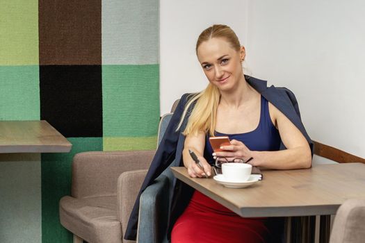 Portrait of beautiful smiling girl holding mobile phone sitting in cafe.