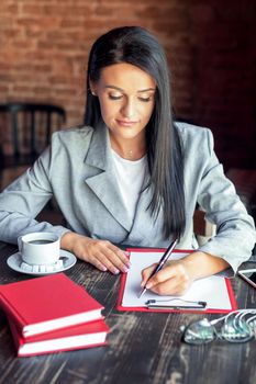 Beautiful young business woman is writing on white paper in the cafe.