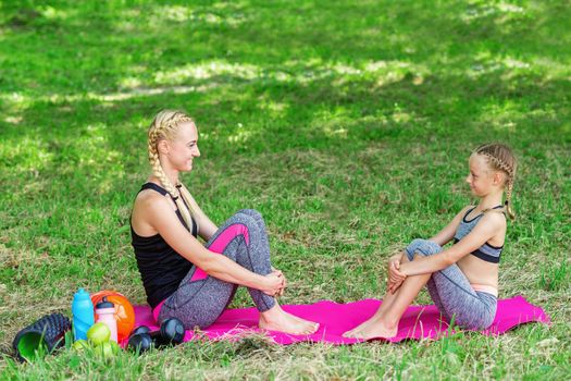 Mother and her daughter sitting on a roll mat in the public park.