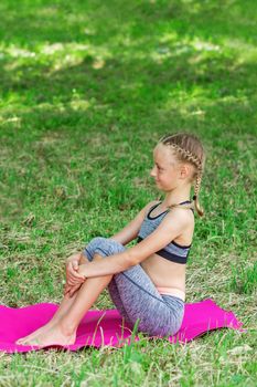 Little girl is sitting on a roll mat wearing sportswear in the public park.