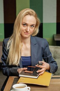 Portrait of beautiful young business woman holding office supplies sitting in office.