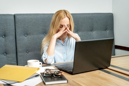 Tired young business woman sitting in front of laptop at office.