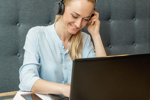 Happy young woman wearing headphones looking on laptop screen during online training and video conference at home office.