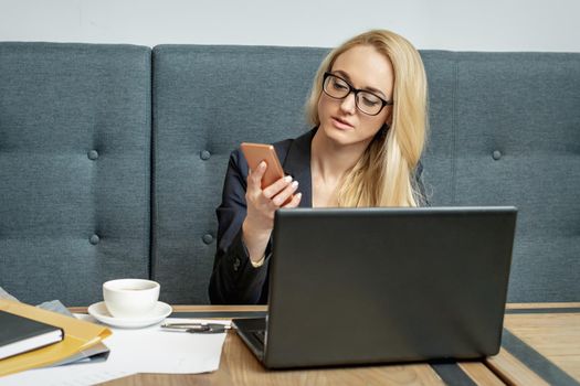 Young business woman is using smartphone sitting at table in cafe.