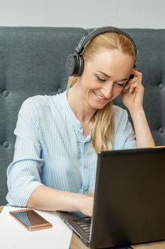 Happy young woman wearing headphones looking on laptop screen during online training with video conferencing at home office.