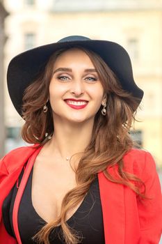 Close up portrait of cheerful white woman in hat with beautiful brown hair smiling at camera on background of city.