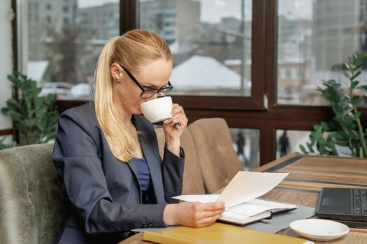 Business woman reading news working with documents and drinking coffee in office.