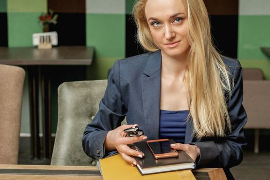 Portrait of beautiful young business woman holding office supplies sitting in office.