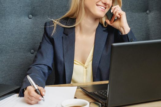 Beautiful young business woman is calling on mobile phone working on laptop in home office.