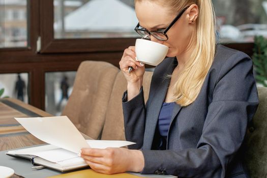 Business woman reading news working with documents and drinking coffee in office.