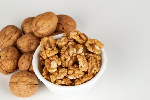 Bowl of walnut kernel with whole walnuts in the background