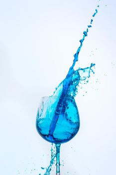 A splash of blue liquid in a glass on a white background. Cutout.