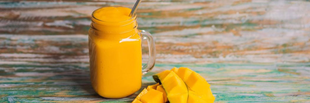 Mango smoothie and steel drinking straw on a painted wooden background. BANNER, LONG FORMAT