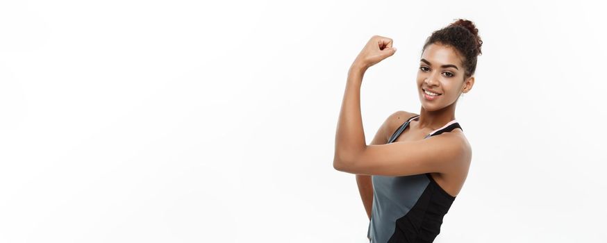 Healthy and Fitness concept - Portrait of young beautiful African American showing her strong muscle with confident cheerful facial expression. Isolated on white studio background