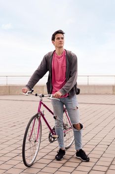 vertical photo of a handsome young man walking with a vintage bike, concept of sustainable transportation and urban lifestyle