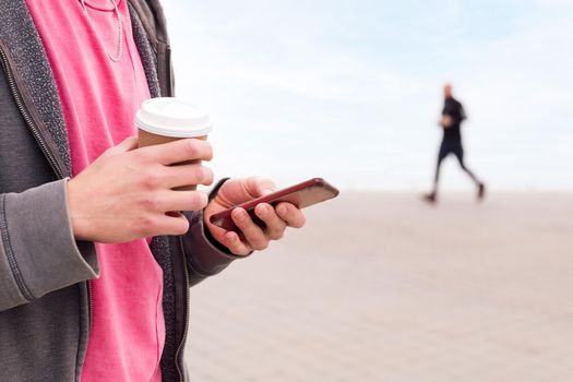 detail of the hands of a young man holding smart phone and coffee outdoors, concept of communication and urban lifestyle, copy space for text