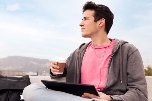 young man sitting outdoors with coffee using a tablet, concept of technology and urban lifestyle, copy space for text, copy space for text