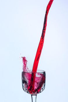 A splash of red wine in a glass on a white background. Cutout.